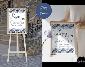 May include: A framed sign with the words "Welcome to Lori's Snow in Love Bridal Shower" in a stylish font. The sign has a floral design with blue and white flowers. The sign is displayed on a wooden easel.