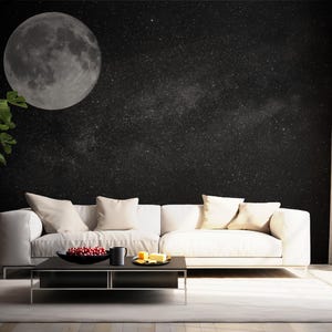May include: A modern living room featuring a white sofa with beige pillows, a black coffee table, and a large wall mural depicting a moon and starry night sky. A potted plant and window with curtains are also visible.