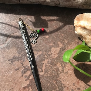 May include: Black and white hair stick with a decorative design. The stick has a gold chain with a heart charm and colorful beads.