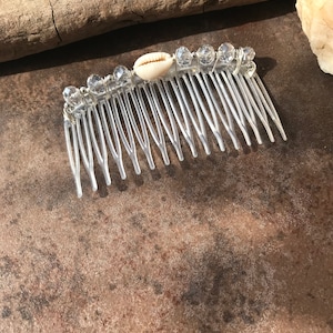 May include: A clear plastic comb with a white seashell and clear beads attached to the top.