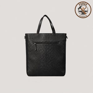 May include: A black tote bag with a textured snakeskin pattern, featuring two top handles and a horizontal zippered pocket on the front. The bag includes a circular logo in the top right corner with the text Forge Leather Co. and an anvil icon.