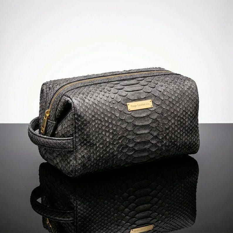 Pode incluir: Uma bolsa de viagem cinza com textura de pele de cobra, z&iacute;per e al&ccedil;a dourados. A bolsa tem formato retangular com uma pequena etiqueta dourada que diz "Forge Leather Co."