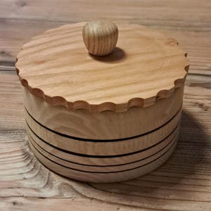 May include: A wooden box with a lid and a knob on top. The box has a scalloped edge and is decorated with black stripes.