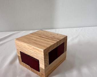 Peut inclure: Un casse-tête en bois en forme de cube avec une finition en bois naturel et des inserts en bois rouge. Le cube est composé de plusieurs pièces qui peuvent être réorganisées pour créer différents motifs.