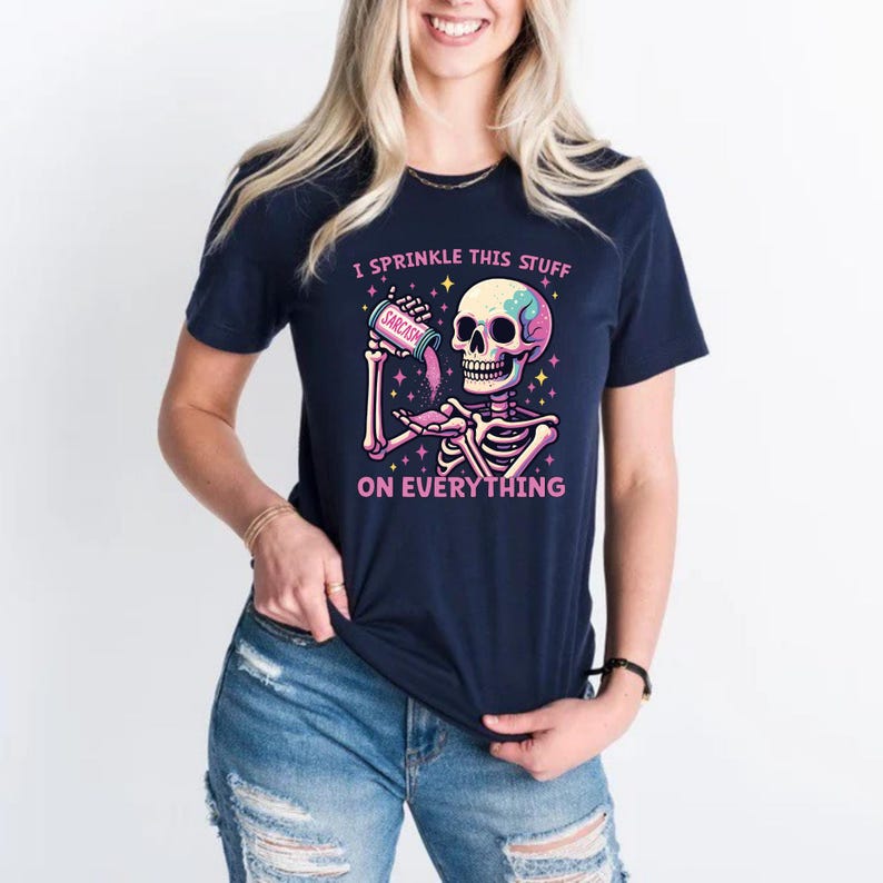 Puede incluir: Camiseta azul marino con un gr&aacute;fico de esqueleto colorido que sostiene un recipiente con la etiqueta "Sarcasmo". El texto de la camiseta dice "Yo esparzo esto sobre todo."