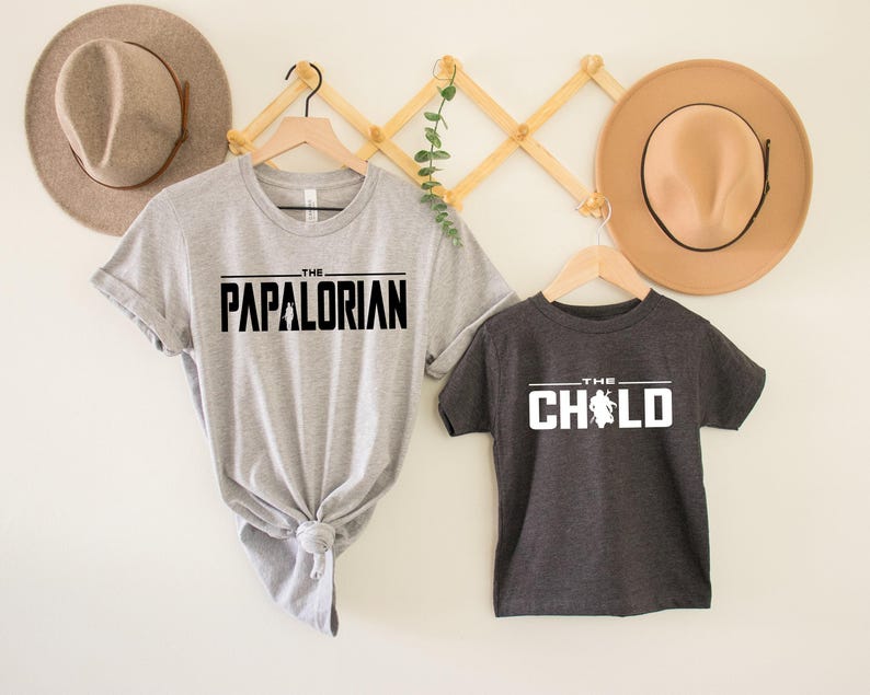 May include: Two gray t-shirts with black text. The larger shirt says "The Papalorian" and the smaller shirt says "The Child" with a stylized image of a baby.