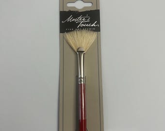 May include: A Master's Touch Fine Art Studio fan brush with a red handle and white bristles. The brush is packaged in a brown cardboard backing with the brand name printed on it.