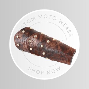 May include: Brown leather arm guard with gold-colored studs. The arm guard is a sleeve-like design with a textured surface. The text "CUSTOM MOTO WEARS" and "SHOP NOW" are visible in a circular design.