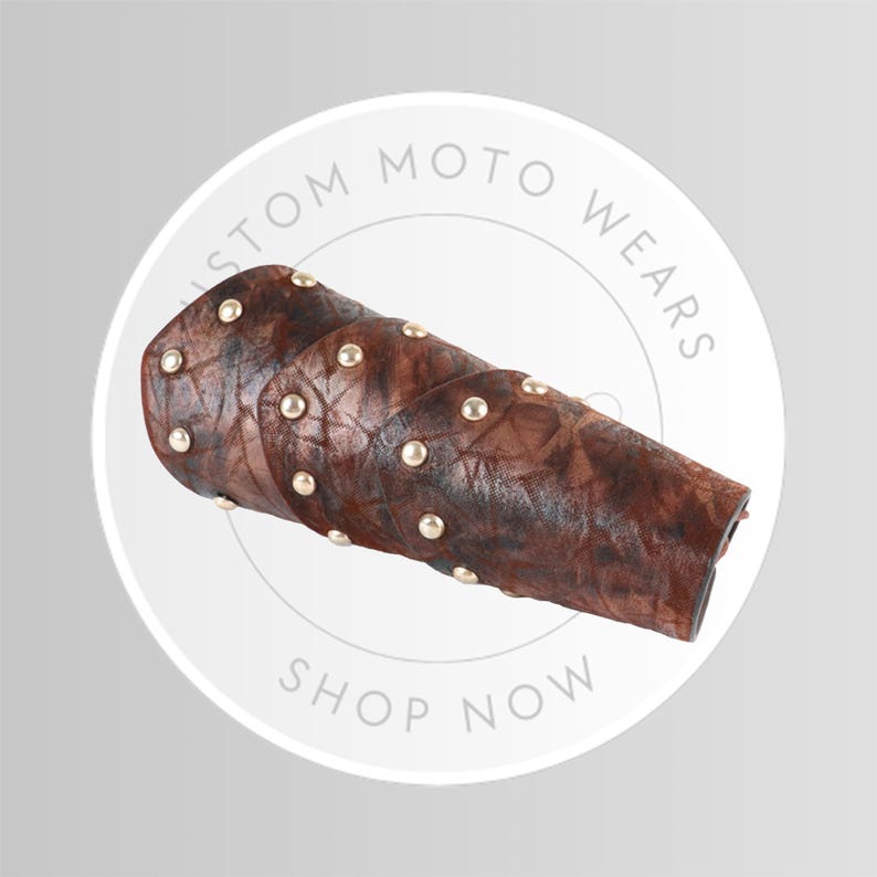 May include: Brown leather arm guard with gold-colored studs. The arm guard is a sleeve-like design with a textured surface. The text "CUSTOM MOTO WEARS" and "SHOP NOW" are visible in a circular design.