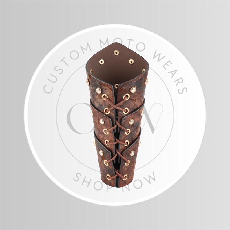 May include: Brown leather arm guard with a textured pattern, laced with brown cord and secured with gold-colored rivets. The arm guard is designed with a pointed top and is likely for protection or fashion. The image includes the text "CUSTOM MOTO WEARS SHOP NOW".