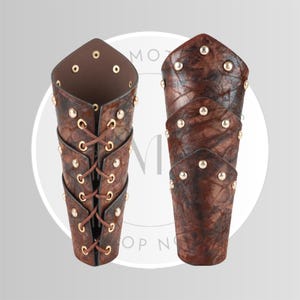 May include: Two brown leather arm guards with gold-colored rivets. One arm guard has a laced closure, while the other is closed. The leather has a textured appearance. The arm guards are designed to protect the forearm.