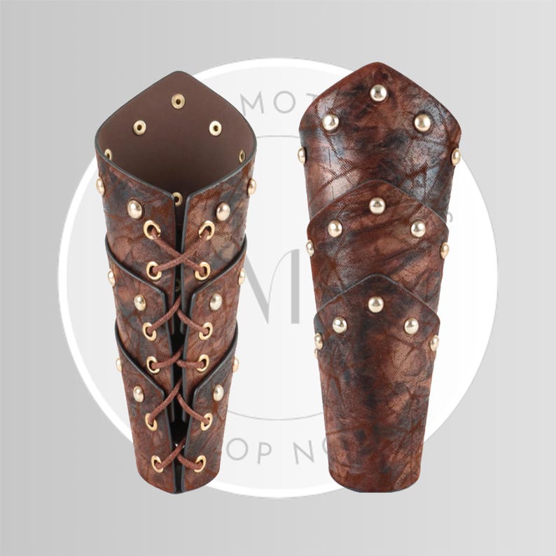 May include: Two brown leather arm guards with gold-colored rivets. One arm guard has a laced closure, while the other is closed. The leather has a textured appearance. The arm guards are designed to protect the forearm.