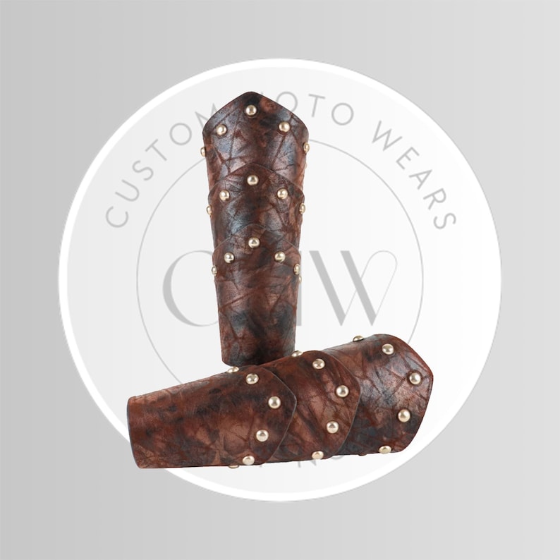 May include: Two brown leather arm guards with gold-colored studs. The arm guards are cylindrical and have a textured appearance. The image includes a white circular logo with the text "CUSTOM MOTO WEARS".