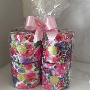 May include: Four rolls of pink and purple floral patterned toilet paper wrapped in clear plastic with a pink satin bow.