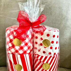 May include: Four rolls of red and white patterned toilet paper wrapped in clear plastic with a red ribbon. Each roll has a gold sticker with a design.