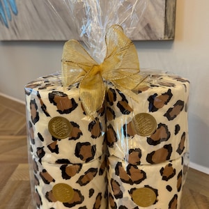 May include: Four rolls of toilet paper wrapped in clear plastic with a gold ribbon. The toilet paper is printed with a leopard print pattern and has a gold seal with the text "Shop The Shelf" on each roll.
