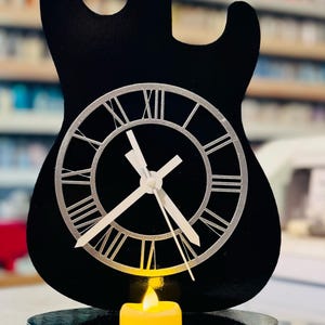 May include: Black electric guitar shaped clock with Roman numeral markings on the face. The clock is on a black base with a small yellow candle.