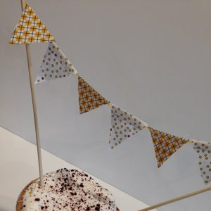 May include: A white and yellow fabric bunting with a checkered and polka dot pattern hangs from a wooden stick. The bunting is strung above a chocolate pie.
