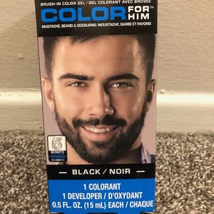 May include: A box of beard and mustache color gel with a 5-minute color application time. The box features a man with a black beard and mustache and the text "COLOR FOR HIM" in blue and white. The box also includes the text "BLACK/NOIR" and "1 COLORANT 1 DEVELOPER/D'OXYDANT 0.5 FL. OZ. (15 mL) EACH/CHAQUE".