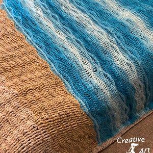 May include: A crocheted blanket with a blue and white wave pattern on one side and a brown pattern on the other side. The blanket is folded in half and the text "Creative Art Expressions" is visible in the bottom right corner.