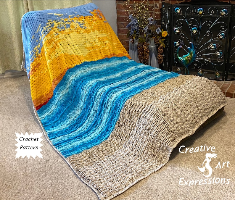 May include: A crocheted blanket with a beach scene design. The blanket features a blue sky, yellow sun, and blue waves. The blanket is draped over a chair and has the text "Creative Art Expressions" on the bottom right corner.