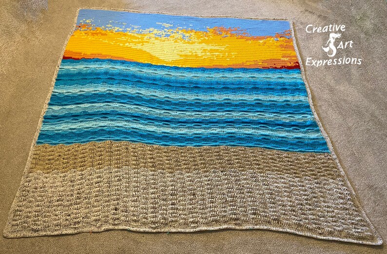 May include: A crocheted blanket with a sunset over the ocean scene. The blanket is made with different shades of blue, yellow, and brown yarn. The blanket is on a gray surface. Creative Art Expressions is written in the top right corner.