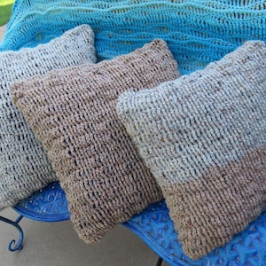 May include: Three crocheted throw pillows in various shades of brown and gray, sitting on a blue bench. The pillows have a textured, open-weave design.  "Crochet Pattern Only" is written in white text on a pineapple graphic.