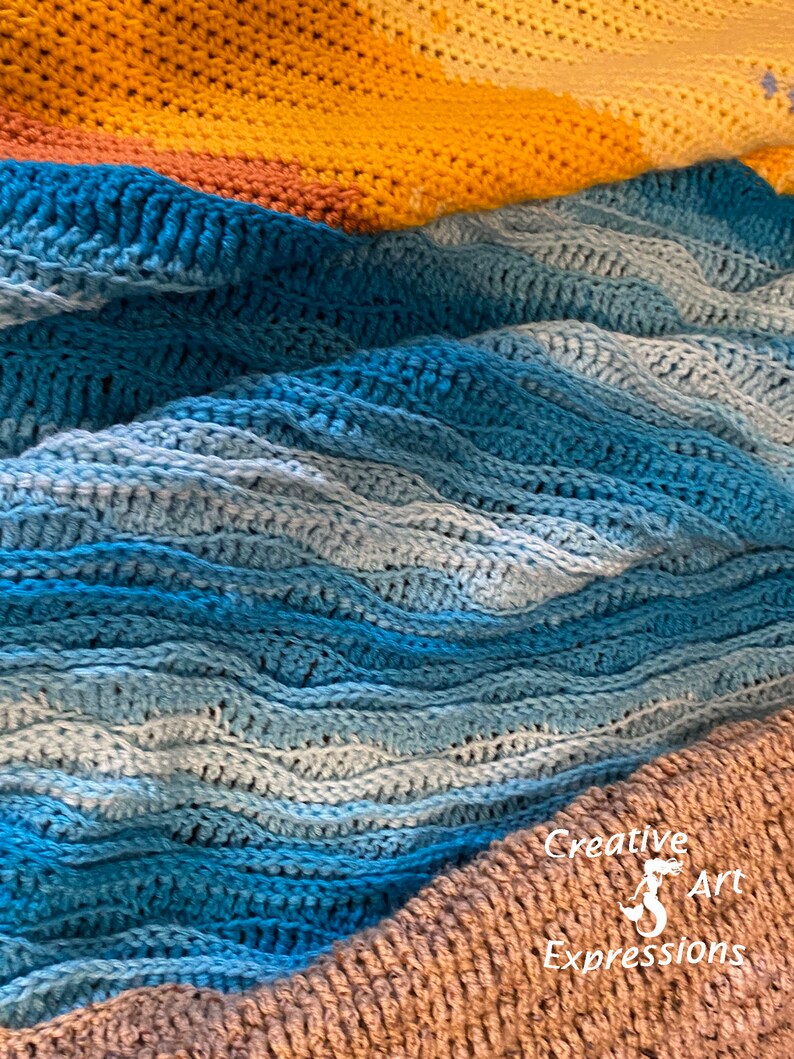 May include: A close-up of a crocheted blanket with a blue and white ombre pattern. The blanket is folded in a wave-like pattern, with a yellow and orange crocheted blanket visible in the background. The text "Creative Art Expressions" is visible in the bottom right corner of the image.