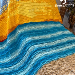 May include: A crocheted blanket with a beach scene. The blanket is made with blue, yellow, and brown yarn. The top of the blanket features a sunset with a blue sky. The middle of the blanket features a blue ocean with waves. The bottom of the blanket features a brown sandy beach.
