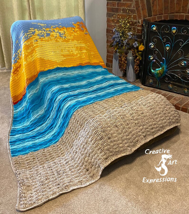 May include: A crocheted blanket with a beach scene. The blanket is made with different shades of blue, yellow, and brown yarn. The blanket is draped over a chair. The text "Creative Art Expressions" is visible in the lower right corner of the image.