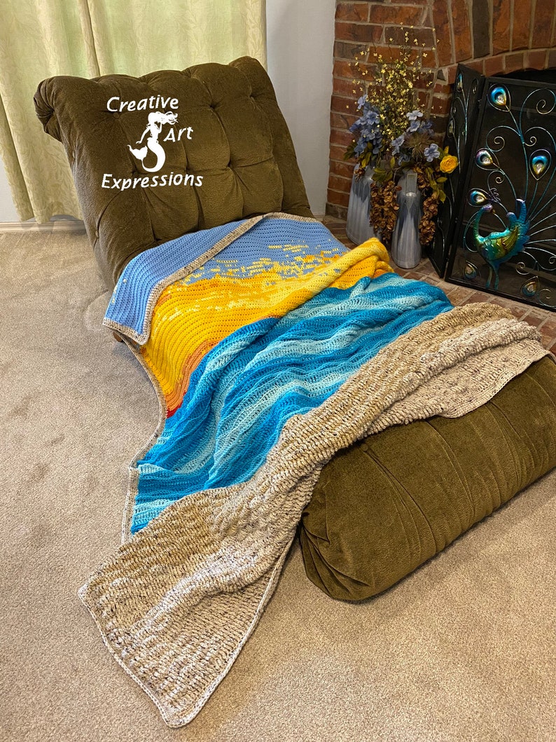 May include: A crocheted blanket with a blue, yellow, and beige color scheme draped over a brown armchair. The blanket has a wave pattern and is made with a variety of textures. The armchair has a tufted back and is in a room with a fireplace.
