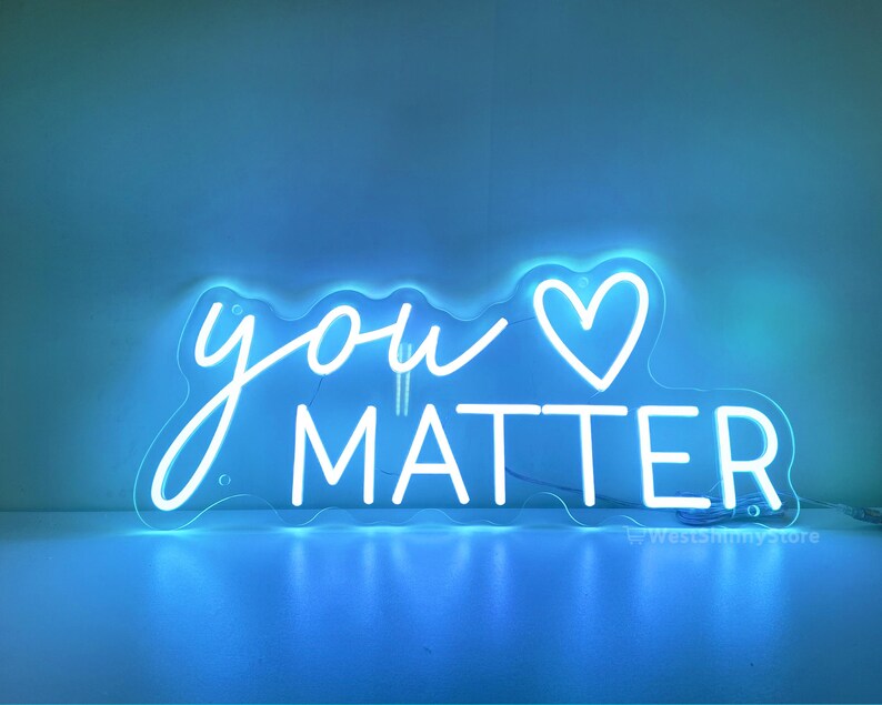 May include: White neon sign with the words "you" and a heart symbol, followed by the word "matter". The sign is lit up and glowing against a blue background.