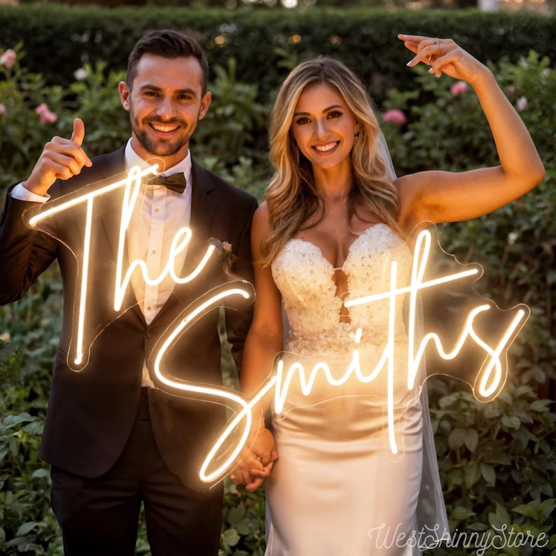 May include: A neon sign with the words "The Smiths" in a cursive font, held by a smiling couple. The sign glows with a warm, inviting light. The background features lush greenery.