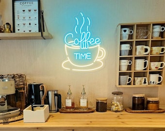 May include: A neon sign in the shape of a coffee cup with the words "Coffee Time" in a light blue glow. The sign is mounted on a wall above a wooden countertop with coffee-making supplies and a shelf with mugs.