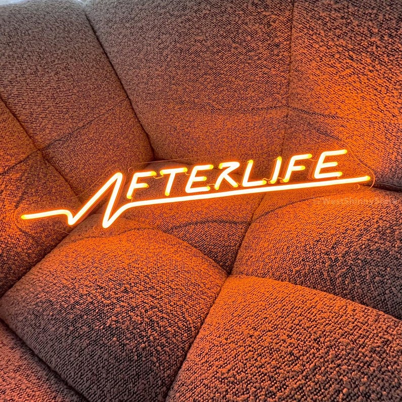 Op de afbeelding: Een neonbord met het woord "AFTERLIFE" in geel-oranje. Het bord staat op een bruin stoffen oppervlak.