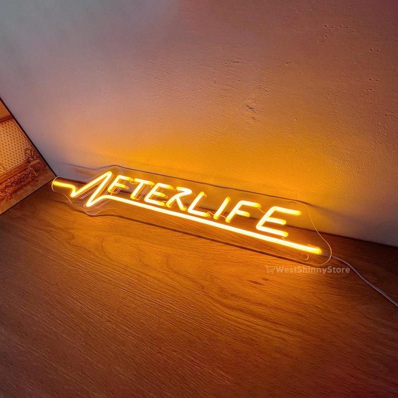 Op de afbeelding: Een neonbord met het woord "AFTERLIFE" in gele neonletters. Het bord is gemonteerd op een doorzichtige acrylplaat.