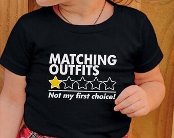 May include: Black t-shirt with the text "MATCHING OUTFITS" in white, and a rating of stars, one yellow and the rest white. Below the stars is the text "Not my first choice!"