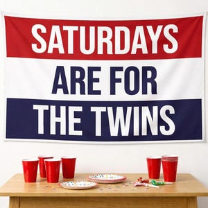 May include: A rectangular wall tapestry featuring horizontal red, white, and blue stripes with the text SATURDAYS ARE FOR THE TWINS printed in bold white and dark blue lettering across the center of the fabric banner.