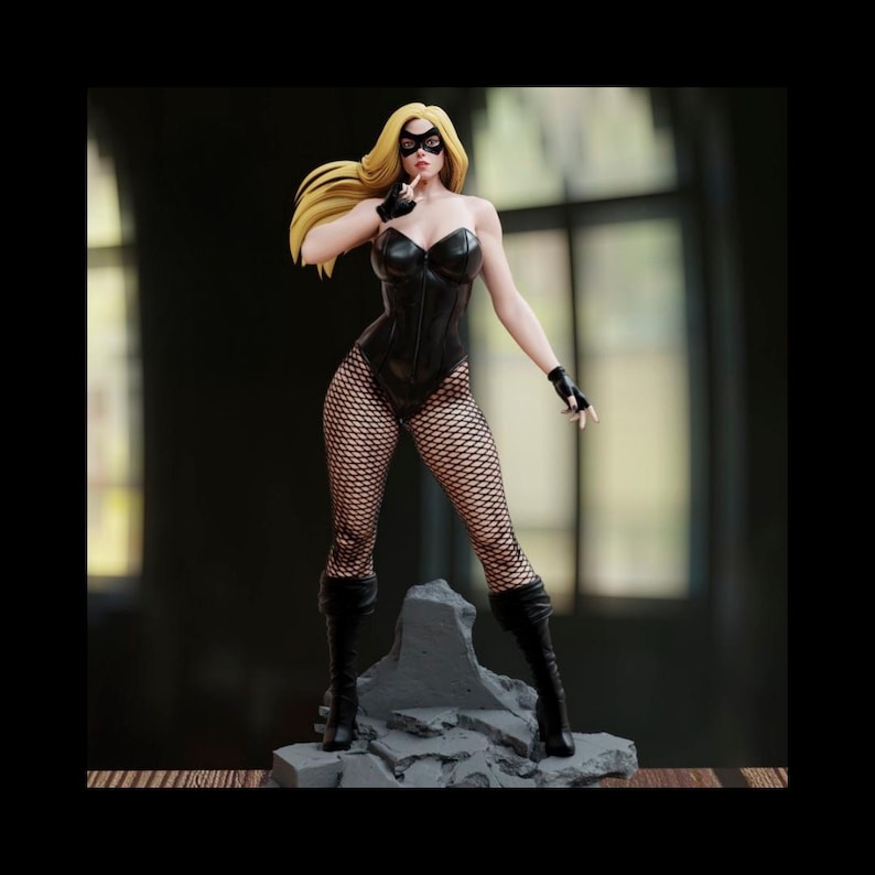 May include: A figurine of a female superhero with long blonde hair, wearing a black bodysuit, fishnet stockings, boots, and a mask. The figure is posed on a gray, rocky base.