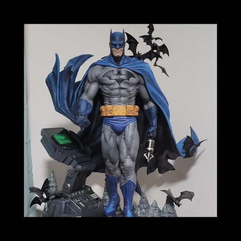 May include: A detailed Batman statue in a dynamic pose, featuring a blue and gray color scheme. The figure has a bat symbol on the chest, a flowing cape, and a utility belt. Several bat-shaped figures are also included.