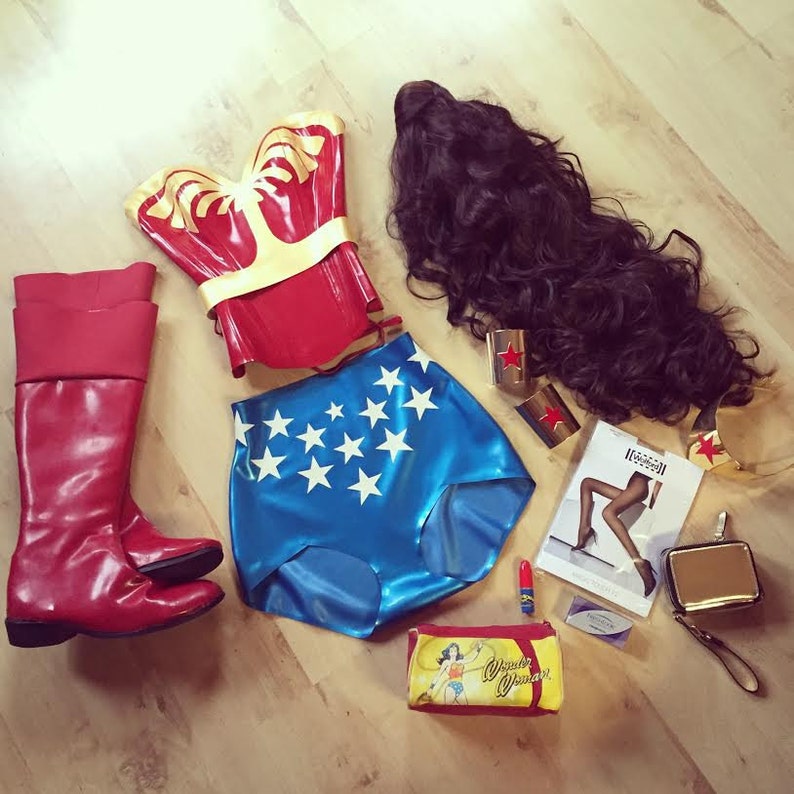 May include: A Wonder Woman costume set, featuring a red and gold corset, blue shorts with white stars, red boots, a black wig, gold wrist cuffs, and a gold purse. A small cosmetic bag with the Wonder Woman logo is also included.
