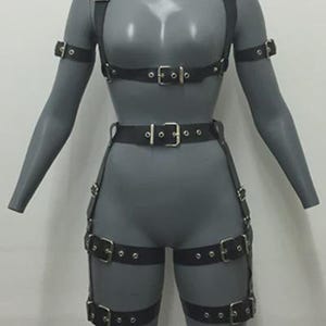 May include: Black leather body harness with multiple straps and silver-colored buckles. The harness includes shoulder straps, armbands, a waist belt, and thigh straps. The product is displayed on a gray mannequin.