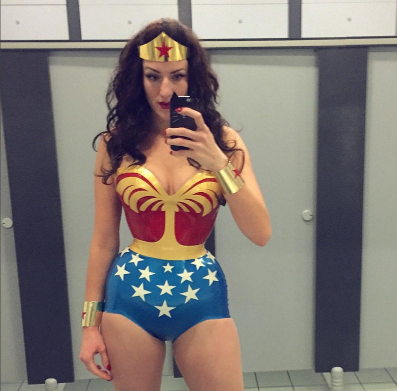 May include: A Wonder Woman costume with a red and gold bodice, blue shorts with white stars, and gold accessories. The costume includes a gold tiara with a red star and gold wrist cuffs. The person is taking a selfie in a bathroom.