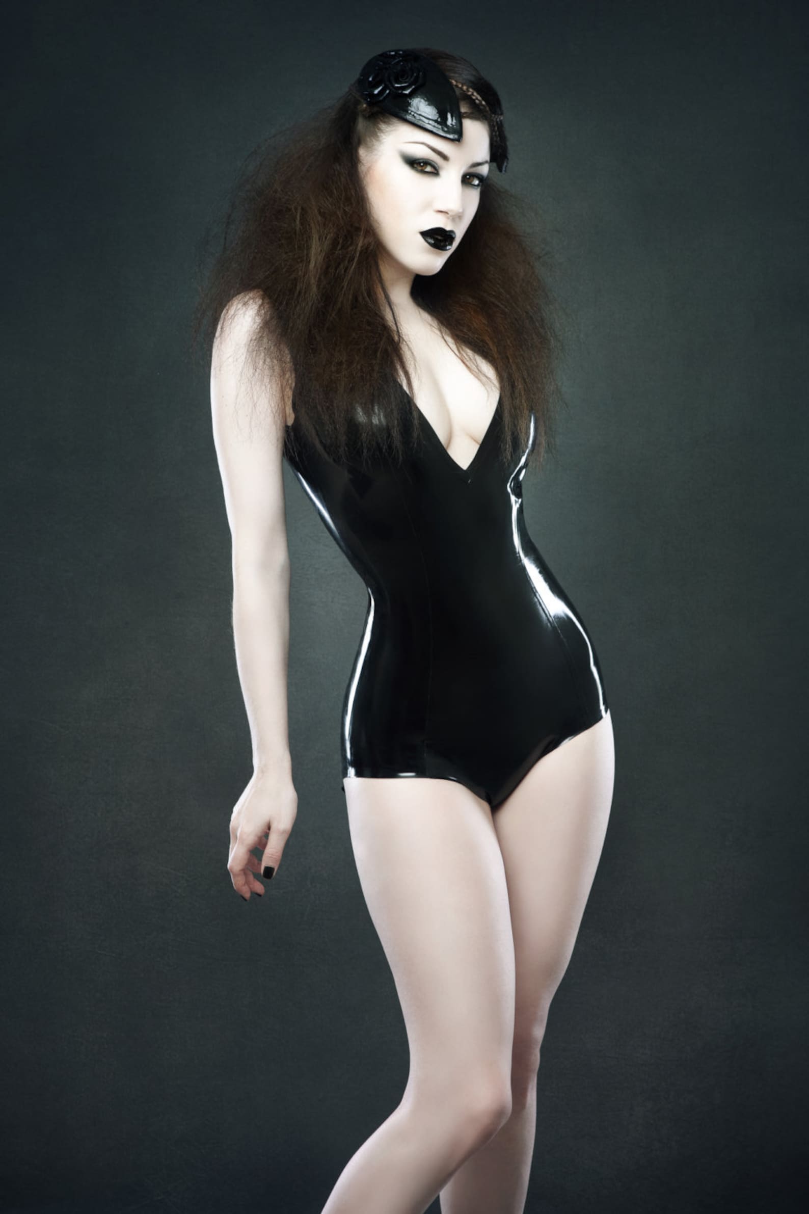 Gothic model in a high-gloss black latex bodysuit with deep V neckline, dramatic teased hair, black lipstick, and a glossy black headpiece.