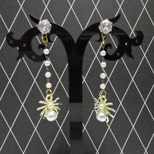 May include: A pair of gold spider earrings with pearl accents and clear crystal tops.