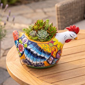 May include: A ceramic chicken-shaped planter featuring a vibrant, multi-colored floral and feather pattern in shades of blue, yellow, orange, and purple. The planter is filled with a variety of green and reddish-toned succulent plants.