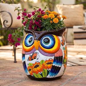 May include: A ceramic owl-shaped planter featuring a white base with hand-painted orange sunflowers, a monarch butterfly, and blue-tipped wings. The owl has large blue and yellow eyes and a yellow beak, filled with vibrant magenta and orange flowers.