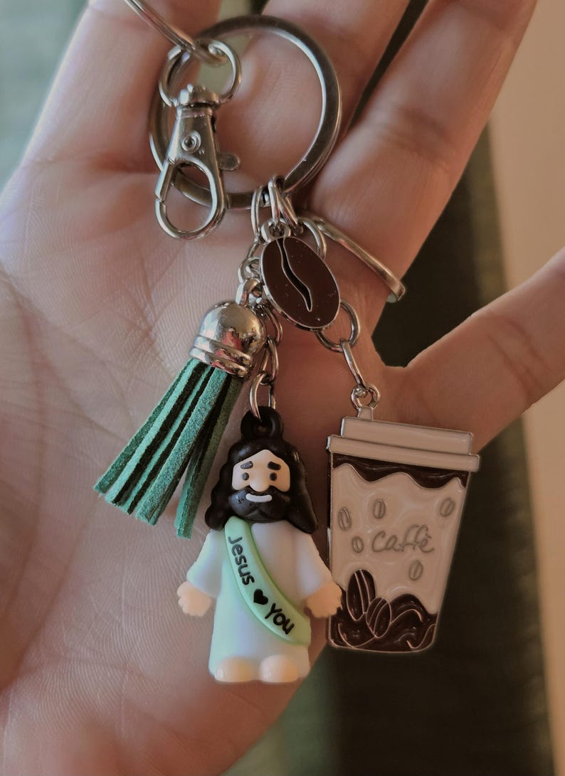 May include: A silver keychain with a green tassel, a coffee bean charm, and two decorative charms. One charm is a small figure of Jesus with the text "Jesus &hearts; You". The other is a coffee cup with the word "Caff&egrave;".