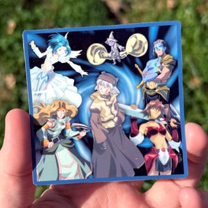May include: Square sticker featuring anime-style characters in various poses, set against a blue background with a swirling design. The sticker has a blue border and is held in a hand against a backdrop of green grass.