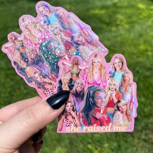 May include: A pink sticker with multiple images of a pop star and glitter details. The sticker has the text "she raised me" in white. The background is green grass.